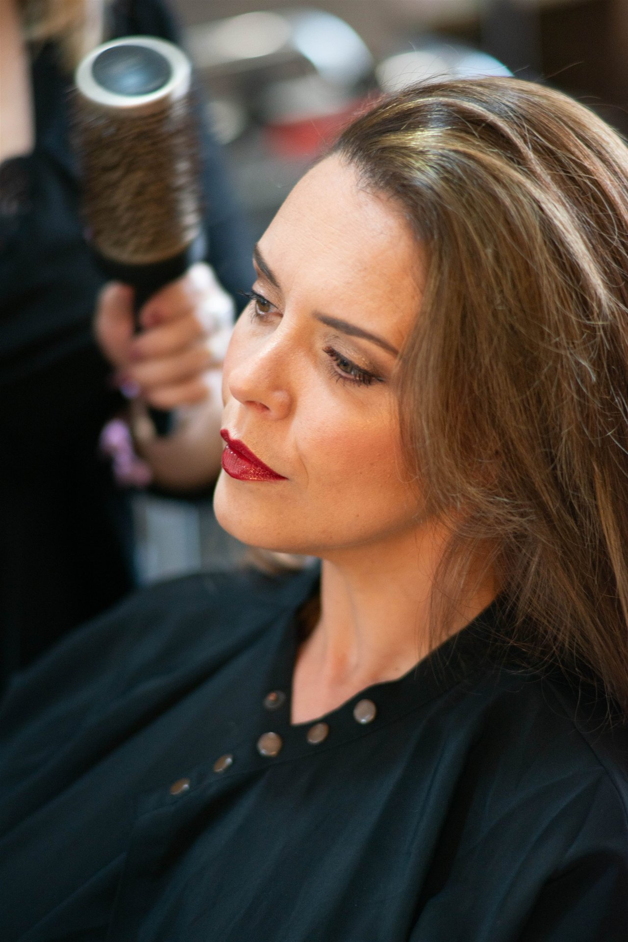 Portrait d'Amandine maquillée pendant la coiffure — lumière chaude du salon, regard tourné