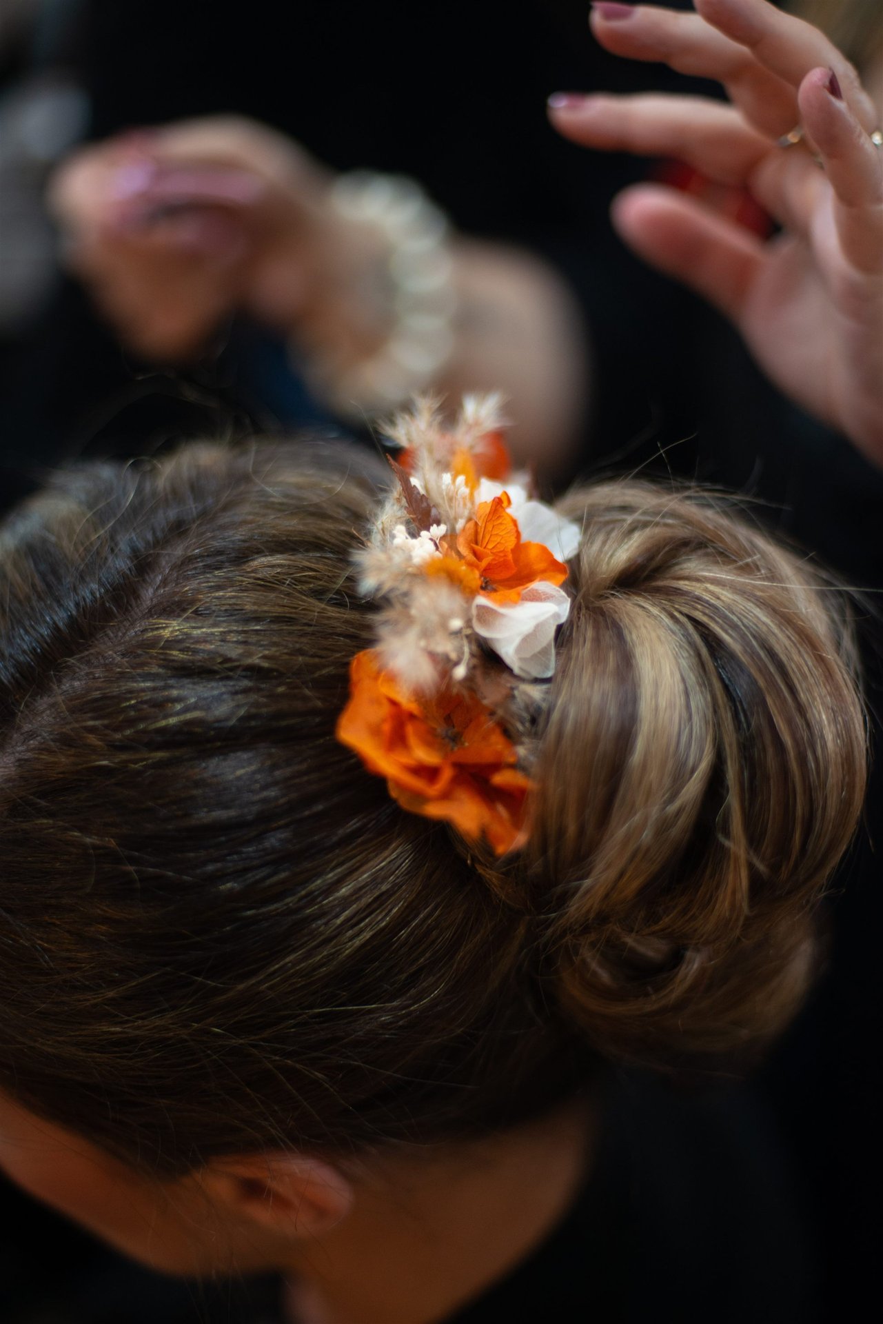 Gros plan de la composition florale de Mille Fleurs Sauvages dans le chignon — fleurs oranges et blanches