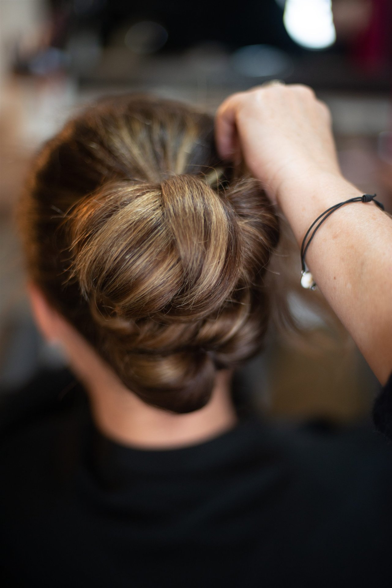 Vue de dos du chignon finalisé — mains d'Annabel effectuent les derniers ajustements — coiffure mariage