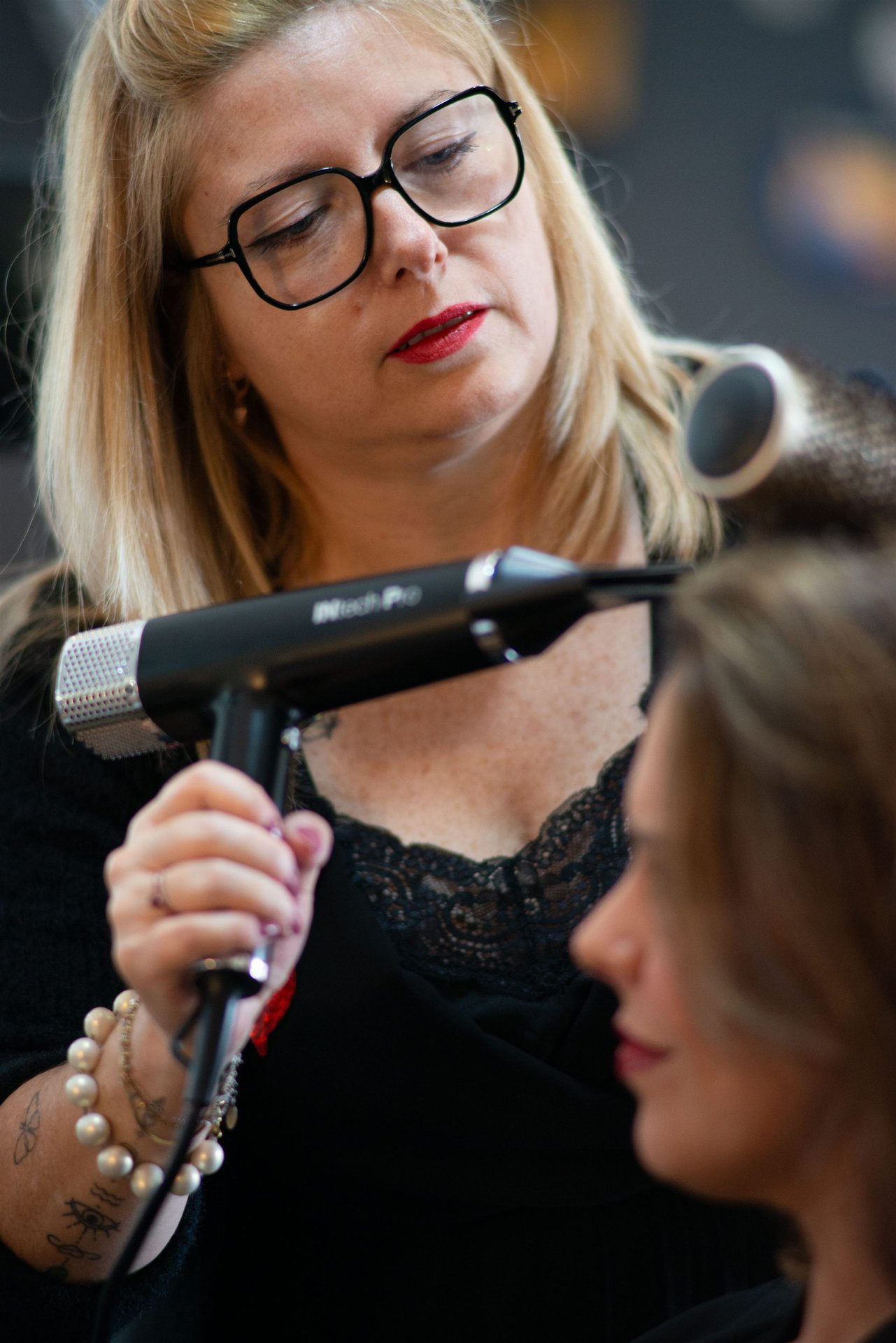 Portrait de la coiffeuse Annabel, lunettes et rouge à lèvres rouge, concentrée avec son sèche-cheveux — Salon D'Ana Perpignan