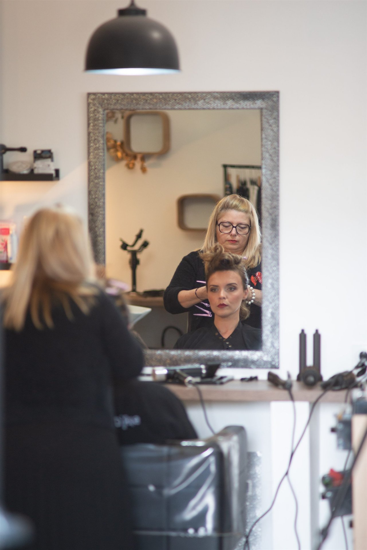 Annabel travaille le chignon d'Amandine, vue dans le grand miroir encadré du Salon D'Ana Perpignan