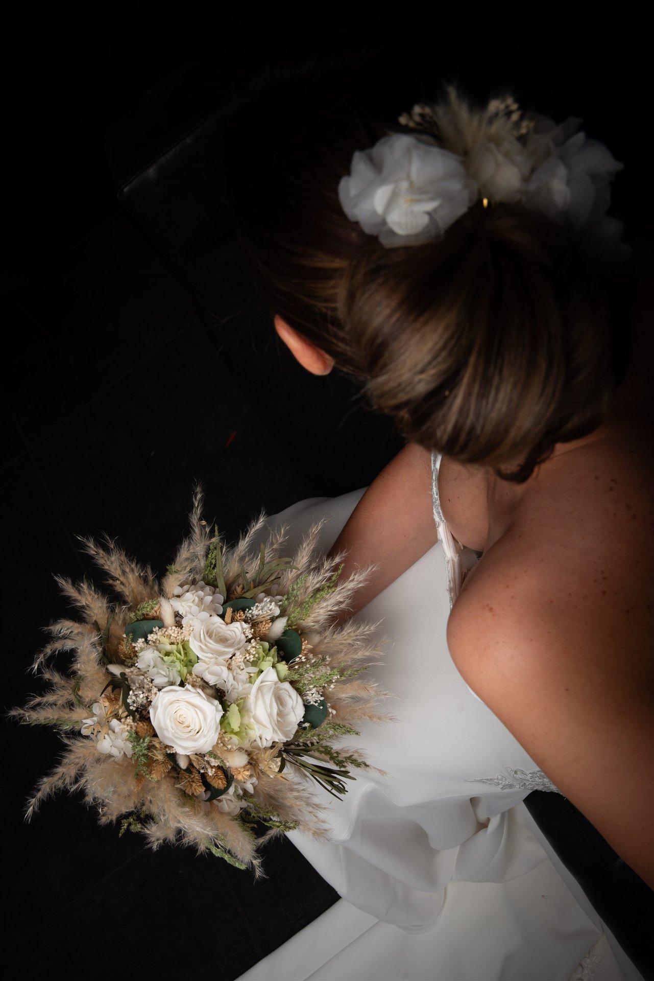 Vue plongeante de dos : chignon de mariée avec fleur, bouquet de roses blanches et pampas — coiffure mariage Perpignan